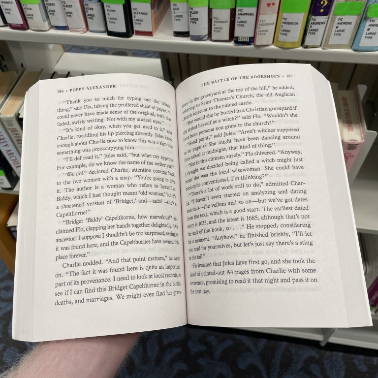 An open book held up in front of a library shelf labelled LARGE TYPE, its pages set in noticeably large text.