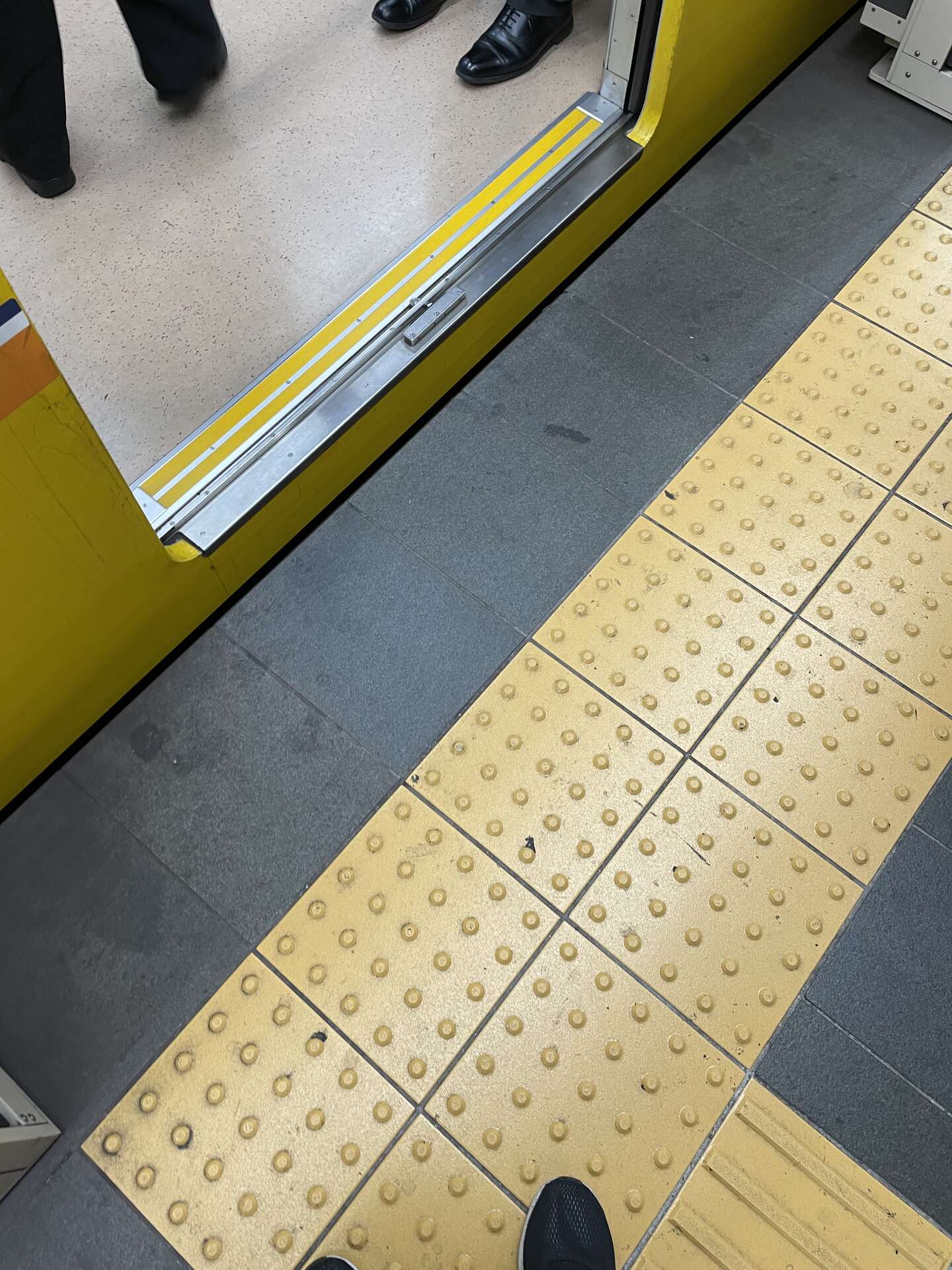 The gap between a train door and the platform, with a line of yellow bumpy tactile paving running alongside the platform edge.