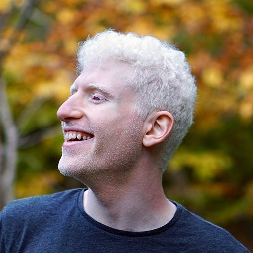 Yotam Sechayk smiling, outdoors, with autumn leaves behind him